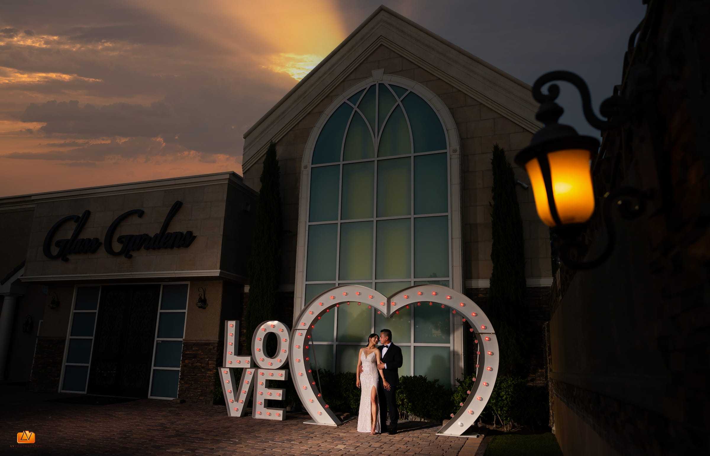 Bride and groom standing inside the illuminated LOVE heart sign outside Chapel of the Flowers in Las Vegas at sunset