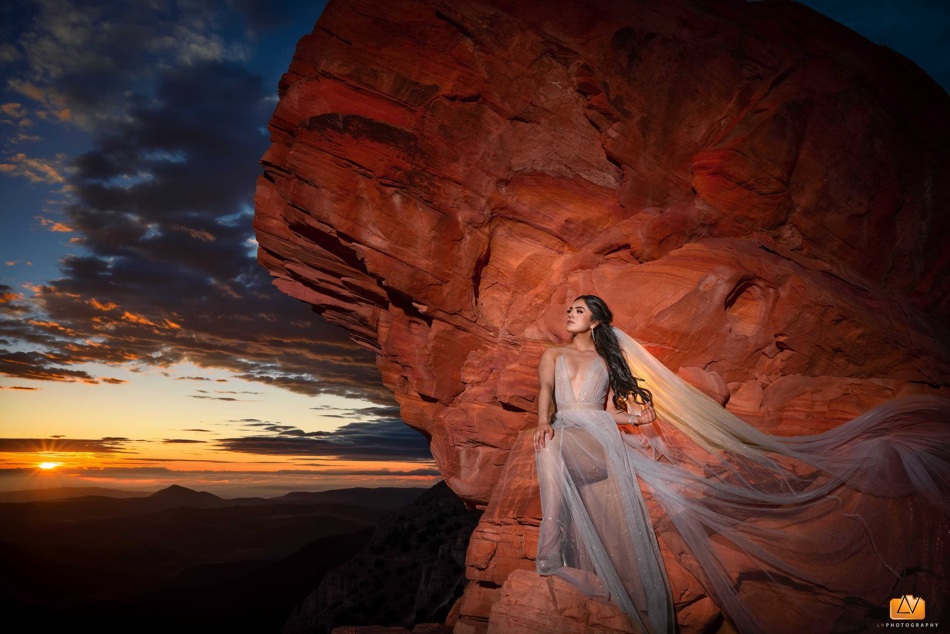 Bride in a flowing wedding dress standing against red sandstone cliffs at Valley of Fire during sunset