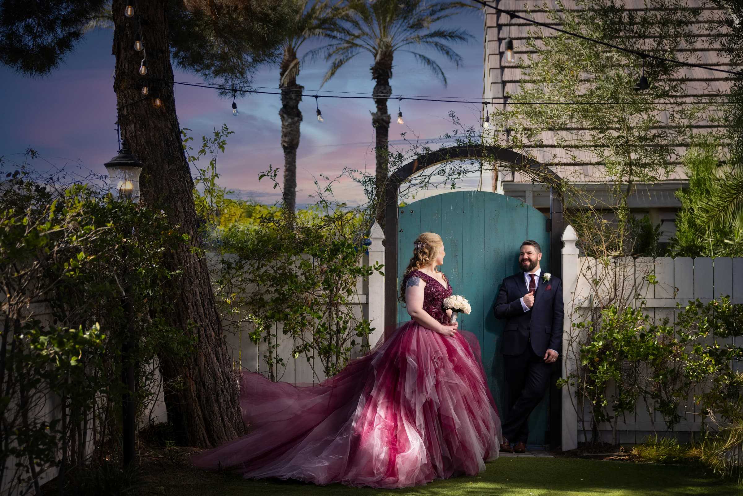 Bride in a pink wedding dress and groom posing by a garden gate at Chapel of the Flowers in Las Vegas