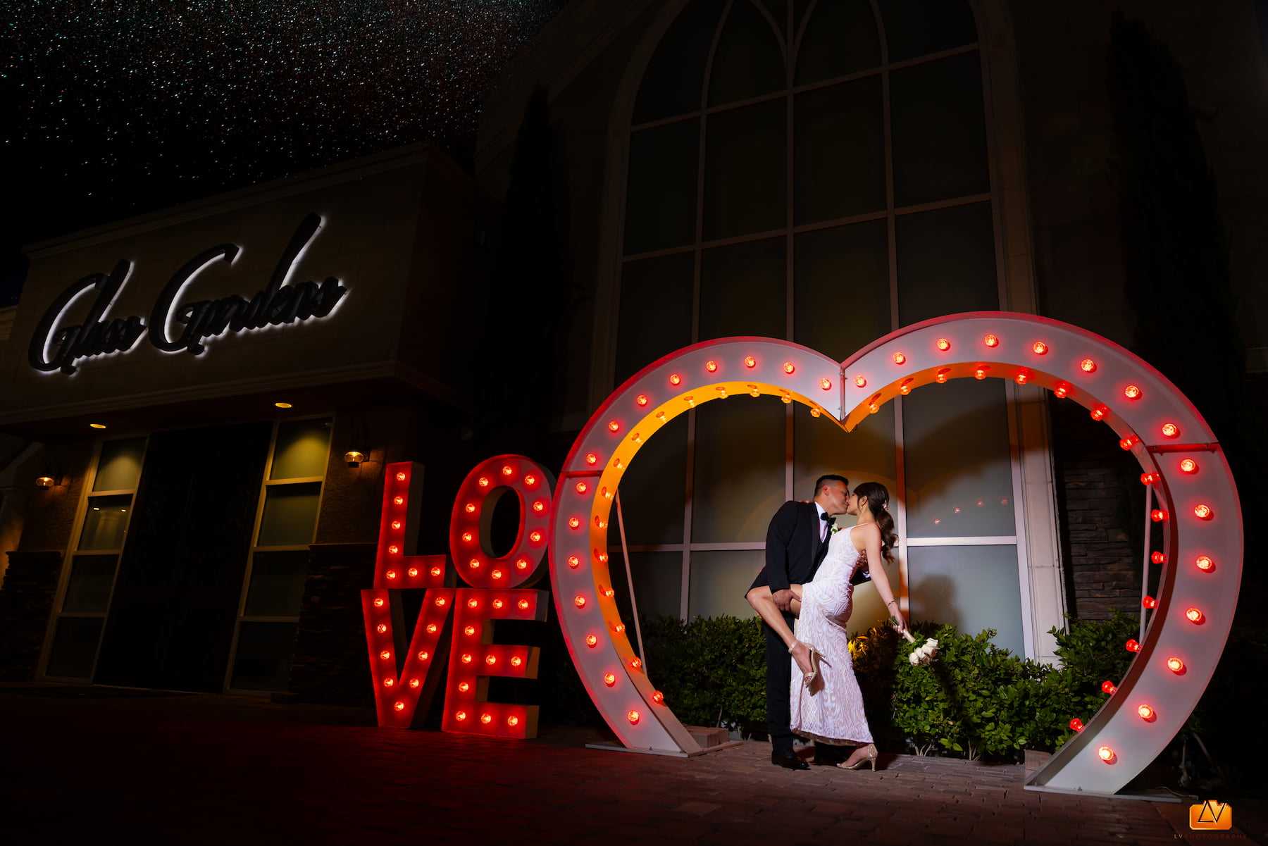 Bride and groom kissing inside the illuminated LOVE heart sign outside Chapel of the Flowers in Las Vegas at night