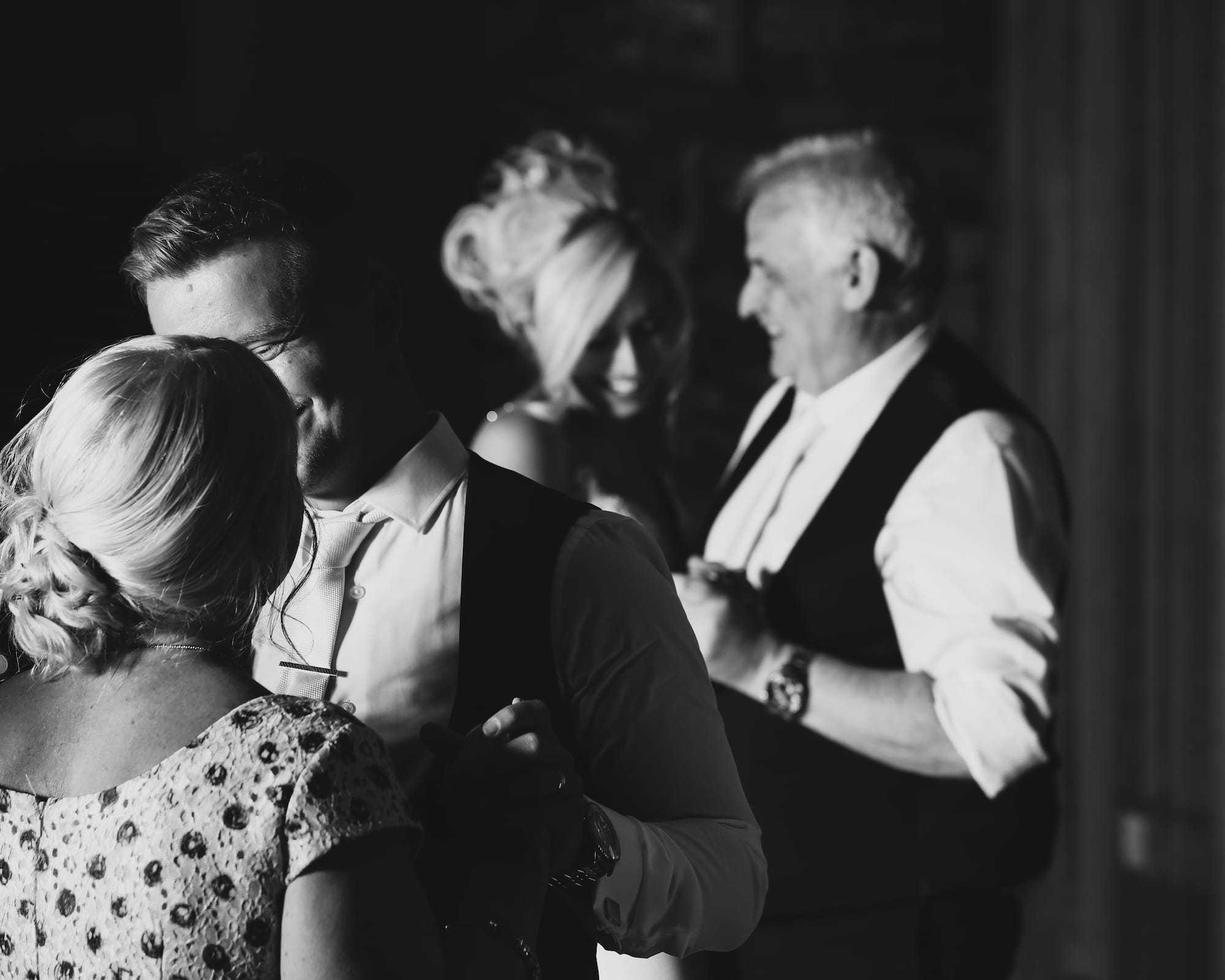 Black and white candid wedding reception photo of guests dancing during an emotional celebration
